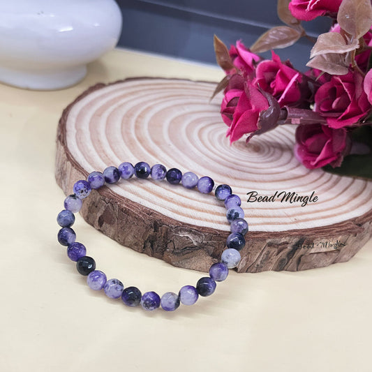 Purple beaded bracelet on a wooden block with pink flowers in the background add bead mingle name back side and make more fresh this
